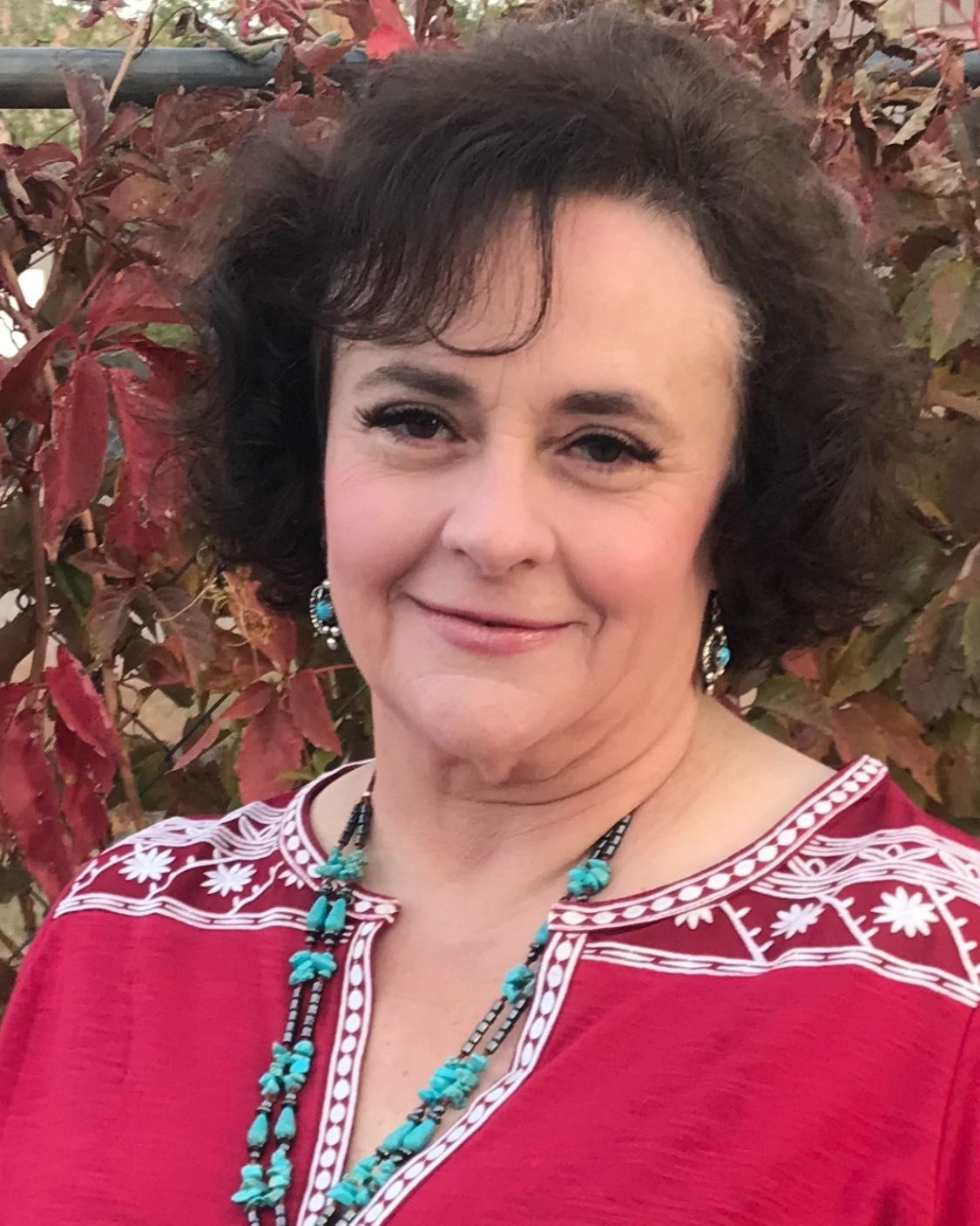 Joanne Yarrish, a certified nurse-midwife, smiling outdoors in front of red autumn leaves.